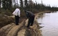 Two hunters analyzing tracks in the sand near a lake