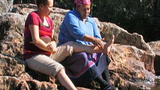 Near a river, a grandmother massages her pregnant granddaughter’s feet