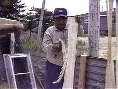 À l'aide d'une hache, un homme fend une planche de bois pour en faire une rame