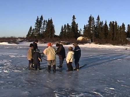 Sur la glace d'un lac en début d'hiver, on s'apprête à percer un trou pour pêcher