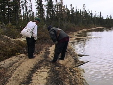 Deux chasseurs en train d'analyser des pistes dans le sable, près d'un lac