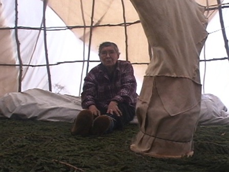 Inside a tent, a woman inspects the installation used to smoke a caribou hide
