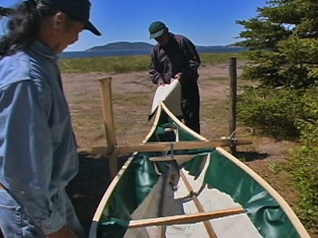 Two men adjust the outer shell of a traditional canoe