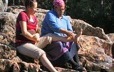 Near a river, a grandmother massages her pregnant granddaughter’s feet