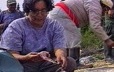 By a fire, a woman dresses a partridge before cooking it