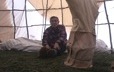 À l'intérieur d'une tente, une femme inspecte l'installation servant à boucaner une peau de caribou