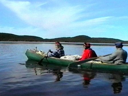 Three Innu row across a lake in a traditional canoe