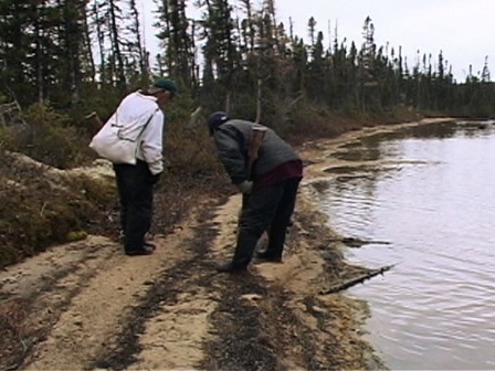 Two hunters analyzing tracks in the sand near a lake