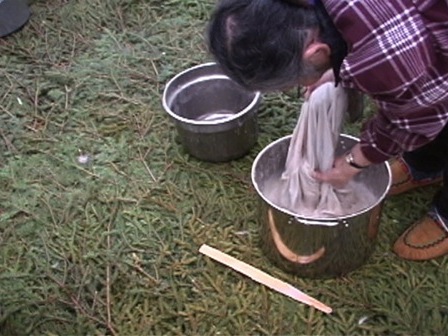 À l'intérieur d'une tente, une femme trempe une peau de caribou pour la tanner